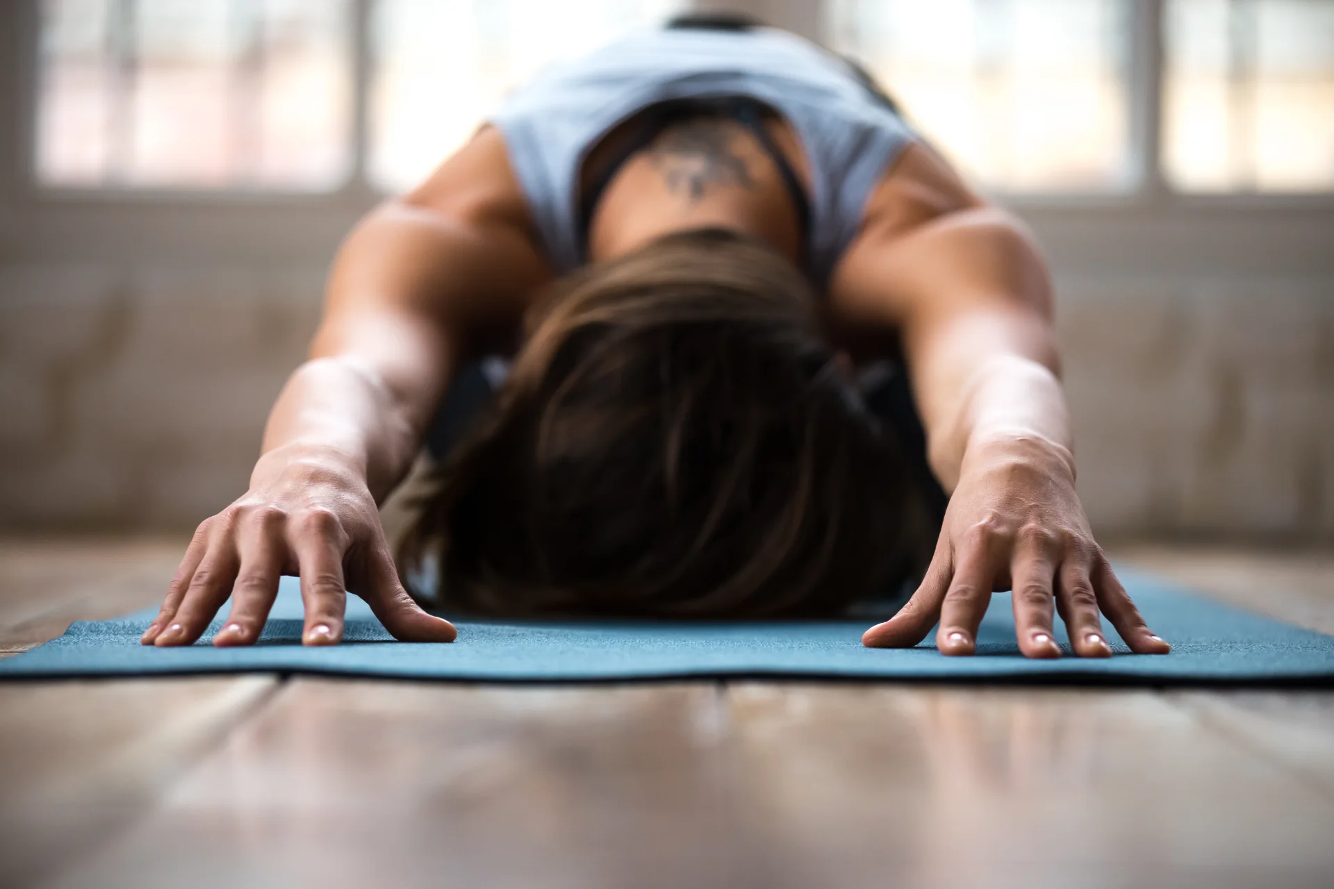 Woman stretching forward with arms extended on a blue yoga mat.