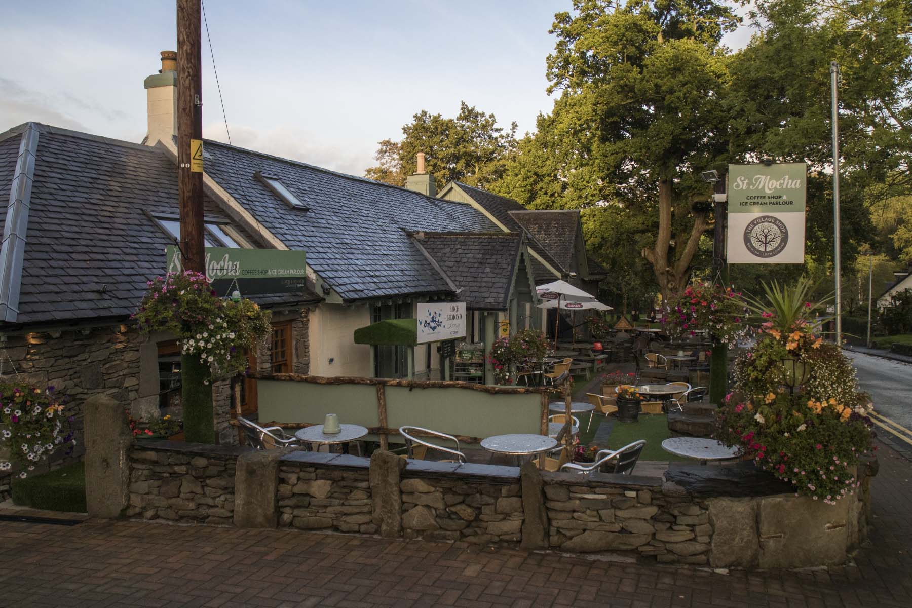 Outdoor tables and hanging flower baskets outside St Mocha cafe in Balmaha.