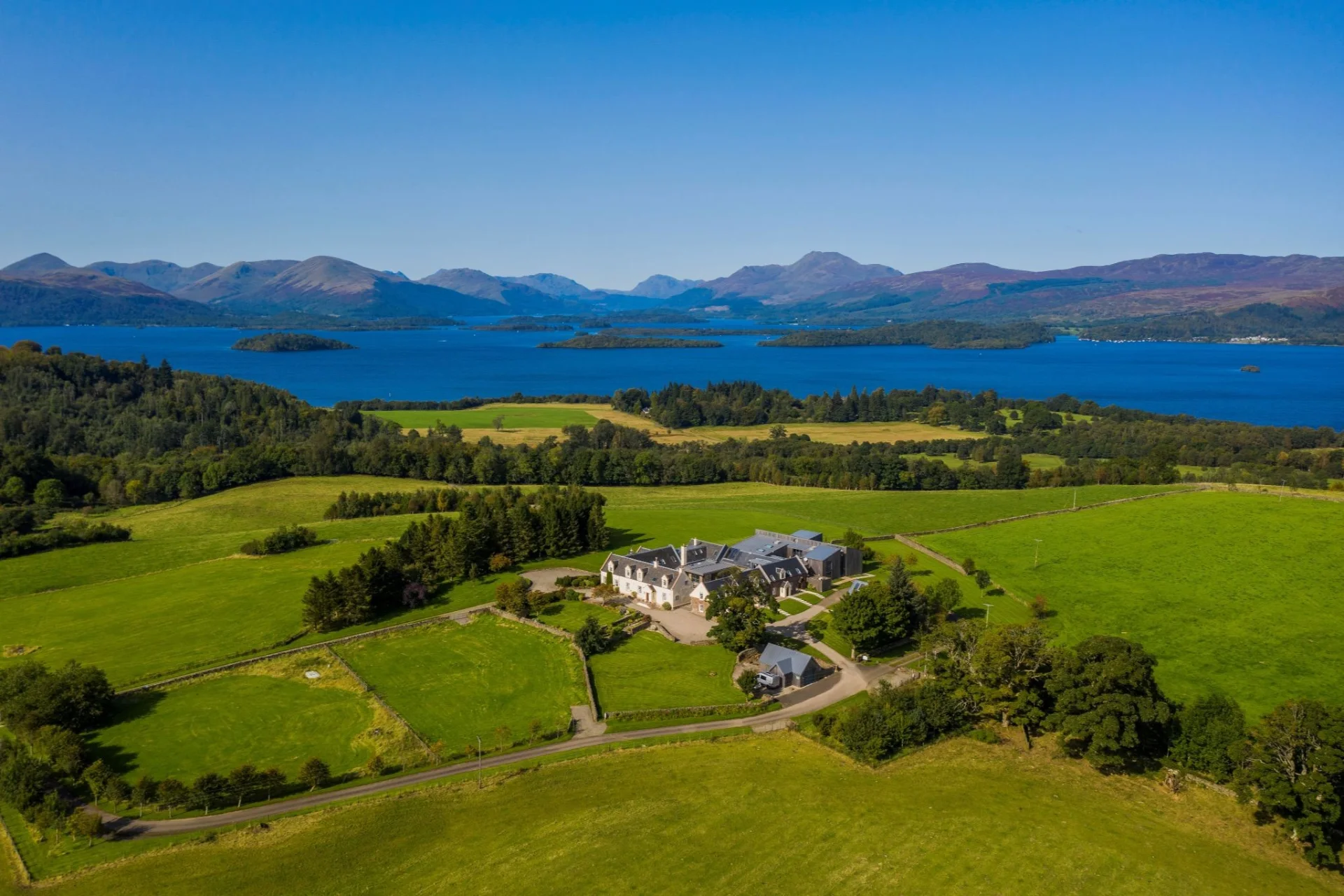 Aerial view of Ardoch Estate, green fields and Loch Lomond with mountains beyond