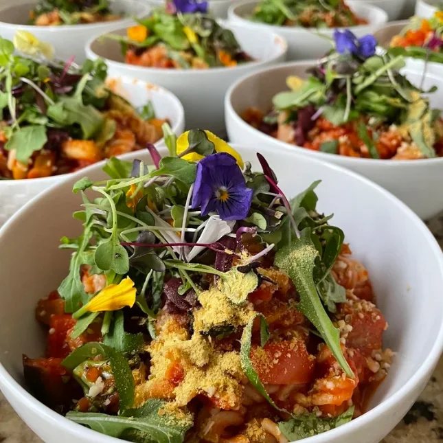 White bowls of colorful food topped with leafy greens and flowers.