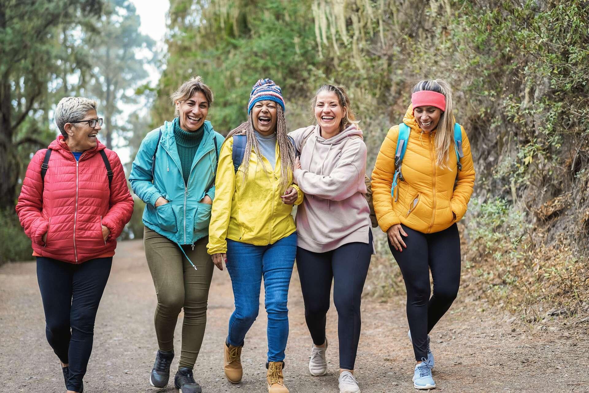 Five women laughing together on a woodland path.